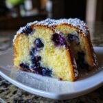 Zwei Scheiben saftiger Lemon Blueberry Bundt Cake, best&auml;ubt mit Puderzucker, auf einem wei&szlig;en Teller.