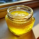 Nahaufnahme eines kleinen Glases gef&uuml;llt mit leuchtend gelber Lemon Vinegarette Dressing, das im Sonnenlicht gl&auml;nzt.