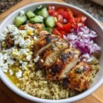 Aufgeschnittenes gegrilltes H&auml;hnchen auf Quinoa in einer Sch&uuml;ssel, garniert mit Feta, Gurken und Zwiebeln im Mediterranean Chicken Bowl.