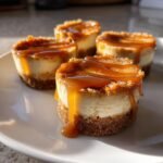 Vier saftige Peanut Butter Karamell Mini Cheesecakes mit dickem Karamell-Topping auf einem wei&szlig;en Teller.