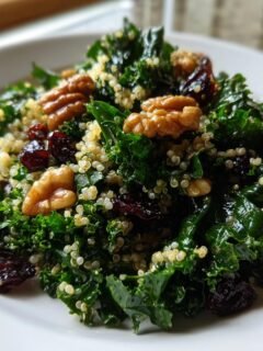 Nahaufnahme eines Protein Packed Kale Quinoa Salat mit Gr&uuml;nkohl, Quinoa, Waln&uuml;ssen und getrockneten Cranberries auf einem wei&szlig;en Teller.