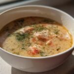 Nahaufnahme einer cremigen Quick Easy Salmon Soup mit Lachsflocken und frischem Dill in einer wei&szlig;en Sch&uuml;ssel.