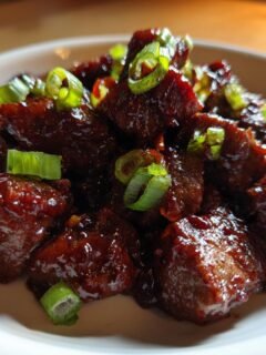 Nahaufnahme von Quick Flavorful Firecracker Steak Bites mit gl&auml;nzender dunkler Glasur und Fr&uuml;hlingszwiebeln.