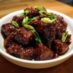 Nahaufnahme von Quick Flavorful Firecracker Steak Bites in einer dunklen, gl&auml;nzenden Glasur, garniert mit Fr&uuml;hlingszwiebeln.