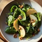 Nahaufnahme eines Quick Healthy Easy Apple Spinach Salad mit frischen Spinatbl&auml;ttern, Apfelscheiben und Waln&uuml;ssen.