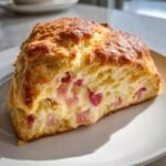Nahaufnahme eines aufgeschnittenen, goldbraun gebackenen Scones mit cremiger F&uuml;llung und rosa Rhabarberst&uuml;cken &ndash; Delicious Rhubarb Custard Scones Recipe.