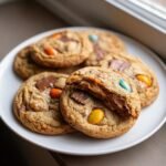Nahaufnahme von weichen Cadbury Egg Cookies, einer davon zerbrochen, mit geschmolzener Schokolade und bunten Eiern.
