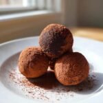 Nahaufnahme von drei unwiderstehlichen Schokoladen-Ricotta-Fudgy-Tr&uuml;ffeln, dick mit Kakaopulver best&auml;ubt.