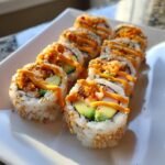 Nahaufnahme von Spicy Volcano Roll Sushi mit Avocado, Sesam und scharfer Sauce auf einem wei&szlig;en Teller.