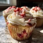 Nahaufnahme eines saftigen Strawberry Shortcake Cupcakes mit wei&szlig;em Frosting und Erdbeerst&uuml;ckchen.