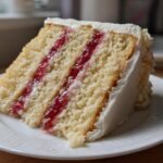 Nahaufnahme eines St&uuml;cks Strawberry Vanilla Layer Cake mit Vanillecreme und roter Marmelade zwischen den B&ouml;den.