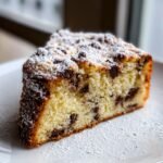 Nahaufnahme eines saftigen St&uuml;cks Irresistible Italian Chocolate Chip Ricotta Cake mit Schokost&uuml;ckchen und Puderzucker.
