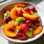 Nahaufnahme eines bunten Summer Peach Fruit Salad mit Pfirsich, Kiwi, Trauben und Mandarinenst&uuml;cken in einer Schale.