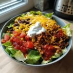 Nahaufnahme einer Sch&uuml;ssel mit Turkey Taco Salad Bowl, belegt mit Hackfleisch, Salat, Mais, Bohnen und Sauerrahm.