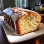 Nahaufnahme eines angeschnittenen, saftigen Key Lime Pound Cake mit dickem Zuckerguss auf einem wei&szlig;en Teller.