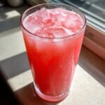 Nahaufnahme eines hohen Glases mit leuchtend rotem Watermelon Lemonade Cooler, gef&uuml;llt mit Eisw&uuml;rfeln.