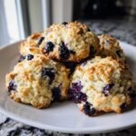Nahaufnahme von fluffigen Zesty Lemon Blueberry Cookies mit vielen Blaubeeren auf einem wei&szlig;en Teller.