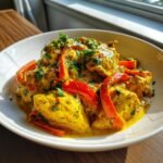 Nahaufnahme von cremigem Coconut Curry Chicken in einer gelben Kokosso&szlig;e mit roten Paprikastreifen und frischer Petersilie.