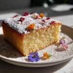 Ein saftiges St&uuml;ck des Elegant Spring Cake With Flowers, best&auml;ubt mit Puderzucker und dekoriert mit bunten essbaren Bl&uuml;ten.
