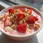 Nahaufnahme eines fertigen Strawberry Smoothie Bowl mit rosa Creme, frischen Erdbeerscheiben und knusprigem M&uuml;sli.