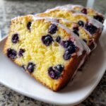Nahaufnahme von drei Scheiben Lemon Blueberry Cake Loaf mit saftigen Blaubeeren und Zitronenglasur auf einem wei&szlig;en Teller.