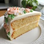 Ein St&uuml;ck Simple Floral Buttercream Cake mit zarter Buttercreme-Blumendekoration auf einem wei&szlig;en Teller.