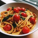 Nahaufnahme einer wei&szlig;en Sch&uuml;ssel mit leckerem Tomato Basil Pasta, garniert mit ganzen Kirschtomaten und Basilikum.